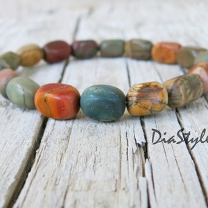 May include: A bracelet made of colorful, natural stone beads. The beads are a mix of red, orange, brown, and green. The bracelet is on a wooden surface.