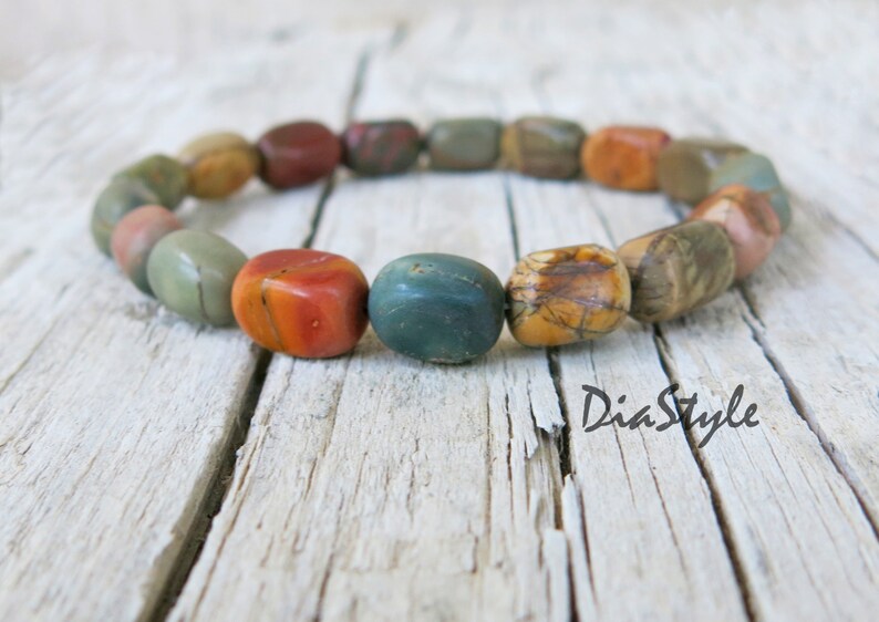 May include: A bracelet made of colorful, natural stone beads. The beads are a mix of red, orange, brown, and green. The bracelet is on a wooden surface.