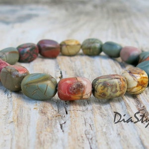 May include: A bracelet made of colorful, oval-shaped stones. The stones are a mix of brown, green, red, and white. The bracelet is on a wooden surface.