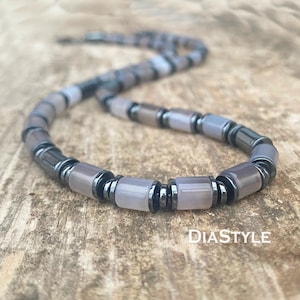 May include: A gray and black beaded necklace with a silver clasp. The beads are round and have a matte finish.