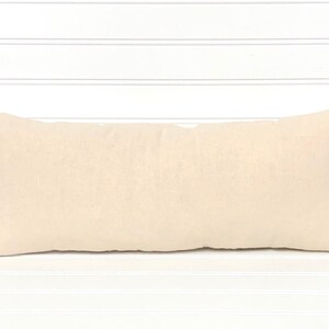 May include: A rectangular, cream-colored pillow with a soft, textured appearance. The pillow is long and narrow, with pointed corners. The neutral color and simple design suggest a focus on comfort and versatility for home decor.