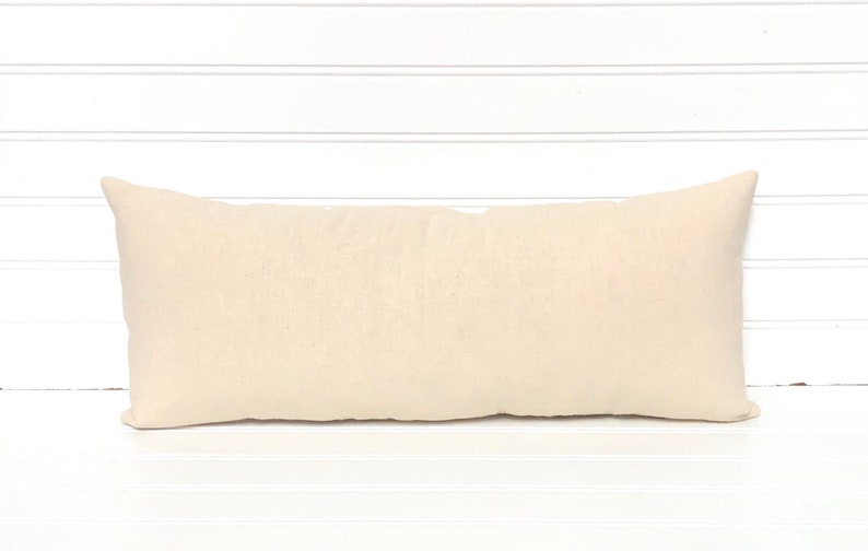 May include: A rectangular, cream-colored pillow with a soft, textured appearance. The pillow is long and narrow, with pointed corners. The neutral color and simple design suggest a focus on comfort and versatility for home decor.