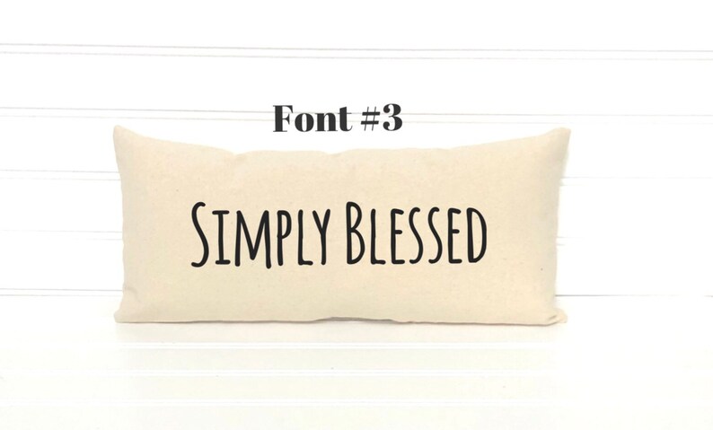 May include: A white pillow with the text "SIMPLY BLESSED" in black font. The pillow is on a white wood background.