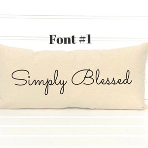 May include: A beige pillow with the text "Simply Blessed" in a cursive font.