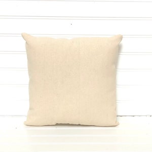 May include: A plain, off-white, square pillow cover made of natural fabric. The pillow cover is sitting on a white surface.