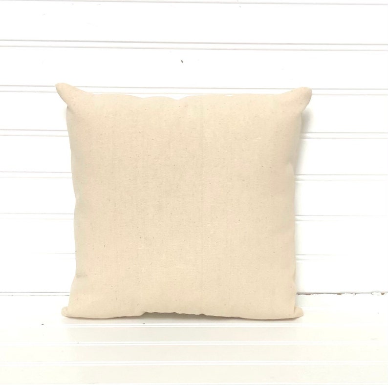 May include: A plain, off-white, square pillow cover made of natural fabric. The pillow cover is sitting on a white surface.