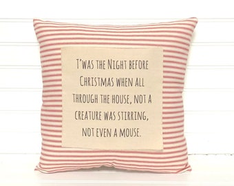 Puede incluir: Cojín cuadrado con un estampado de rayas rojas y blancas. El cojín presenta un parche rectangular con el texto "T'was the Night Before Christmas when all through the house, not a creature was stirring, not even a mouse."