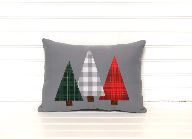 May include: A gray throw pillow with three appliqu&eacute;d Christmas trees. The trees are green, white and red plaid.