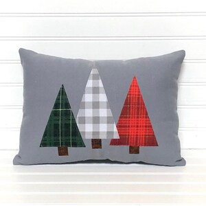 May include: A gray throw pillow with three appliqu&eacute;d Christmas trees. The trees are green, white and red plaid.