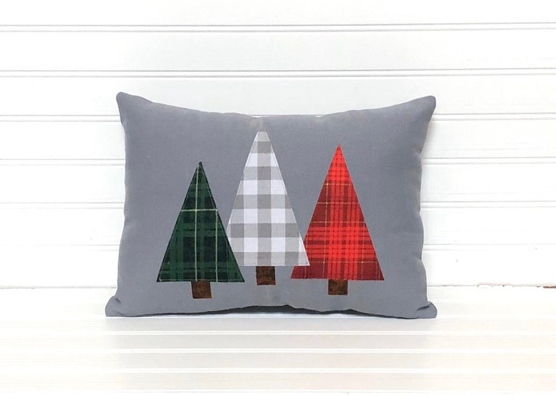May include: A gray throw pillow with three appliqu&eacute;d Christmas trees. The trees are green, white and red plaid.