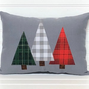 May include: A gray throw pillow with three appliqu&eacute;d Christmas trees. The trees are green, white and red plaid.