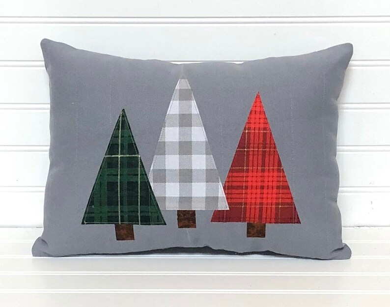 May include: A gray throw pillow with three appliqu&eacute;d Christmas trees. The trees are green, white and red plaid.