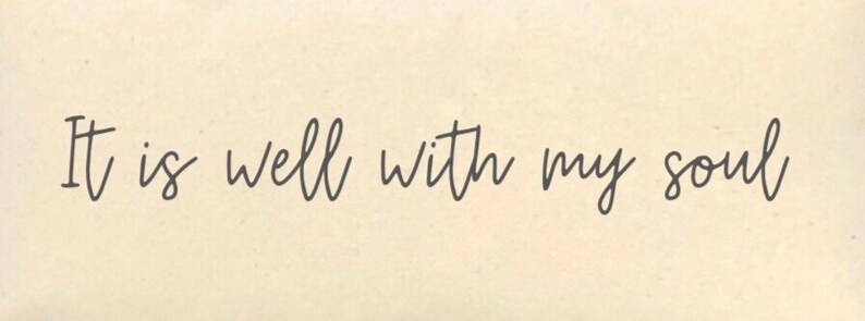 May include: A rectangular sign with the phrase "It is well with my soul" in elegant, dark gray cursive script. The text is centered on a cream-colored background, creating a simple yet impactful design. The sign's aesthetic is clean and suitable for various home decor styles.