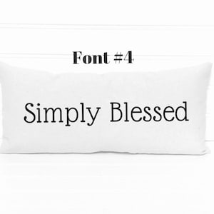 May include: White pillow with the text "Simply Blessed" in black font. The pillow is on a white wood background. Font #4.