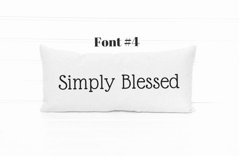 May include: White pillow with the text "Simply Blessed" in black font. The pillow is on a white wood background. Font #4.
