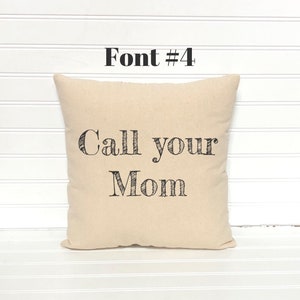 May include: A beige square pillow with the text "Call your Mom" in black, stylized font. Above the text is the text "Font #4" in black. The pillow is on a white surface.