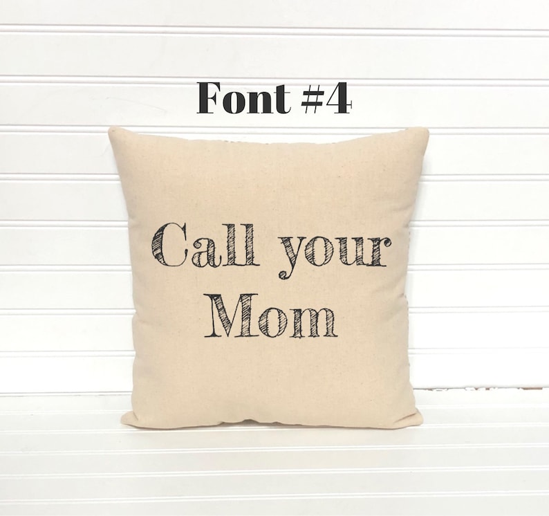 May include: A beige square pillow with the text "Call your Mom" in black, stylized font. Above the text is the text "Font #4" in black. The pillow is on a white surface.