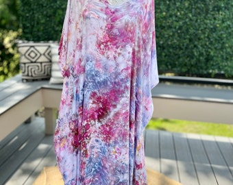 Może przedstawiać: Długa, zwiewna, biała kaftan z dekoltem w kształcie litery V i wzorem tie-dye w odcieniach różowego, fioletowego i niebieskiego.