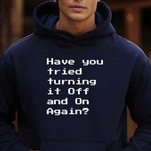 Op de afbeelding: Een marineblauwe hoodie met de tekst "Have you tried turning it off and on again?" in wit.