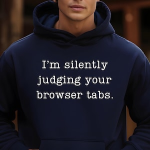Op de afbeelding: Een marineblauwe hoodie met witte tekst die "Ik beoordeel je browsertabbladen stilletjes." zegt.