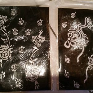 May include: Two black and white stencil sheets for henna or mehndi designs. One sheet features a floral design with roses and leaves. The other sheet features a more intricate design with swirls and flowers.