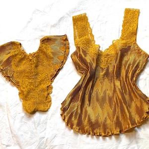Puede incluir: Conjunto de lencería amarillo mostaza. El conjunto incluye una camisola con ribete de encaje y cuello en V, y una parte inferior a juego. La tela tiene una textura plisada. La lencería se muestra sobre una superficie blanca.