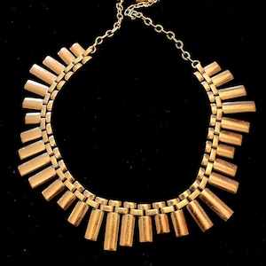 May include: A gold-toned necklace with a geometric design. The necklace is made of a series of connected rectangular pieces that form a fan shape.
