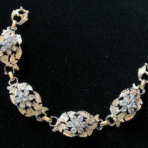 Puede incluir: Un brazalete de plata con un diseño floral y brillantes transparentes. El brazalete tiene un cierre de broche.
