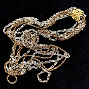 Può includere: Una collana multifilo con una chiusura dorata e un design floreale. La collana è realizzata con catene dorate e argentate.