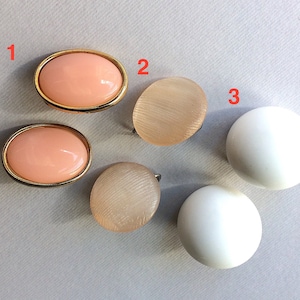 Può includere: Sei paia di orecchini, due paia sono di forma ovale con un centro rosa e un bordo dorato, due paia sono rotondi e di colore marrone chiaro, e due paia sono rotondi e bianchi.