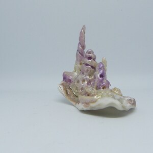 Puede incluir: Una peque&ntilde;a concha blanca con una espiral morada y blanca en la parte superior. La concha es un objeto natural y tiene una textura rugosa.