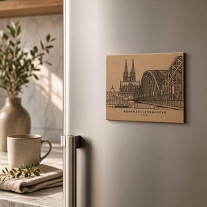 Op de afbeelding: Een rechthoekige beige magneet met een zwarte lijntekening van de Hohenzollernbrücke en de Dom van Keulen. De tekst "HOHENZOLLERNBRÜCKE KÖLN" is in zwarte hoofdletters onderaan het ontwerp op het oppervlak van de magneet gedrukt.