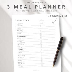 Puede incluir: Un planificador de comidas blanco con una lista de compras, con secciones para cada día de la semana y horarios de comidas. El texto "3 MEAL PLANNER" está en la parte superior. Un bolígrafo negro y dorado descansa sobre el planificador.
