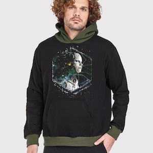 Op de afbeelding: Zwarte hoodie met een groene en witte grafische print van een robotgezicht. De hoodie heeft een groene voering.