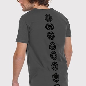 Pode incluir: Uma camiseta cinza-chumbo com uma fileira vertical de sete s&iacute;mbolos de chakras pretos impressos nas costas.