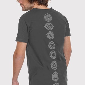 Pode incluir: Uma camiseta cinza-chumbo com uma fileira vertical de sete s&iacute;mbolos de chakras cinzentos impressos nas costas.