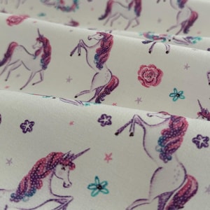 May include: White fabric with a repeating pattern of purple and pink unicorns with flowers and stars.