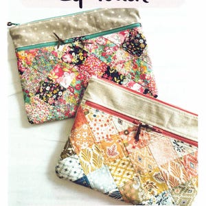 May include: Two patchwork zip pouches with floral and geometric patterns. The pouches have a divided double zip design and are approximately 9 inches by 12 inches. The text "Divided Double Zip Pouch" is at the top.
