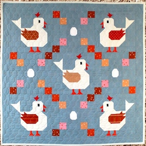May include: A blue quilt pattern with a chicken design. The quilt features white chickens with brown and red accents, surrounded by colorful squares and egg shapes. The pattern is labeled "Scrambled Eggs" and is available in 41.5" x 41.5" and 65.5" x 65.5" sizes.