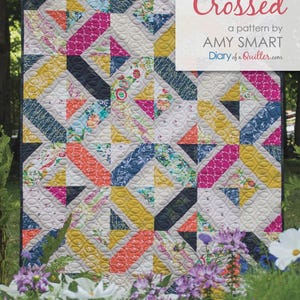 May include: A quilt featuring a geometric pattern of interlocking rectangles and triangles in shades of mustard yellow, hot pink, navy blue, and floral prints on a light gray background with white stippled quilting and the text Double Crossed.