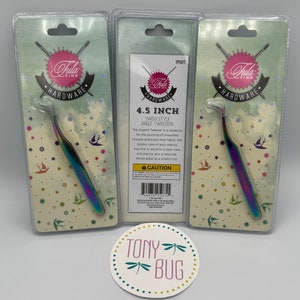 May include: A set of three 4.5 inch angled tweezers in rainbow colors, packaged in clear plastic with a white background featuring a pink and white logo that says "Hula Pink Hardware". The packaging also includes a description of the tweezers and a caution label.