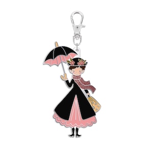 May include: A metal keychain featuring a cartoon character with a black coat, pink dress, and a matching hat with floral accents. The character holds a black and pink umbrella and a yellow bag. The keychain has a silver clasp.