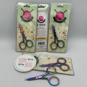 May include: Three packages of 4 inch large ring micro-tip scissors with rainbow colored handles. The scissors are packaged on a white background with a pink and green design. The packaging includes the text "Tula Pink Hardware" and "4 inch".