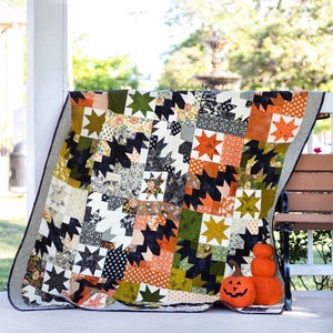 May include: A handmade quilt with a star pattern in various colors, including black, orange, green, and cream. The quilt is draped over a bench, with three decorative pumpkins in front. The quilt's design features a mix of geometric and floral patterns.