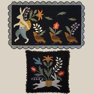 May include: Two black felt wall hangings with a whimsical folk art design. The top hanging features a white rabbit carrying a basket of flowers and three brown birds. The bottom hanging features a white rabbit hopping out of a basket of flowers with a blue bird flying above.