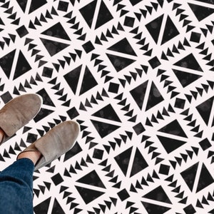 Puede incluir: Suelo con estampado geométrico en blanco y negro con los pies de una persona que lleva zapatos marrones y pantalones vaqueros azules de pie en el suelo.