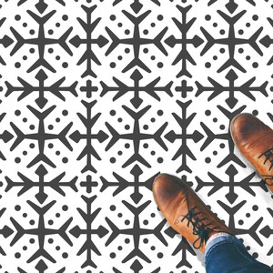 Könnte beinhalten: Ein Paar braune Lederstiefel mit weißen Schnürsenkeln stehen auf einem schwarz-weißen gemusterten Boden. Das Muster ist ein sich wiederholendes geometrisches Design aus Schneeflocken.