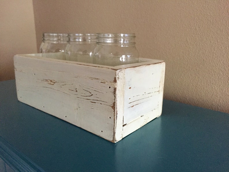 K&ouml;nnte beinhalten: Wei&szlig;e Holzkiste mit abgenutzter Farbe, die vier klare Glasgl&auml;ser enth&auml;lt. Die Kiste steht auf einer t&uuml;rkisfarbenen Oberfl&auml;che.