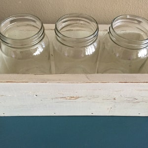 K&ouml;nnte beinhalten: Wei&szlig;e Holzkiste mit drei durchsichtigen Glasbeh&auml;ltern. Die Kiste hat eine wei&szlig;e, abgenutzte Lackierung und ist perfekt zum Pr&auml;sentieren von Blumen oder anderen Dekorationsartikeln.