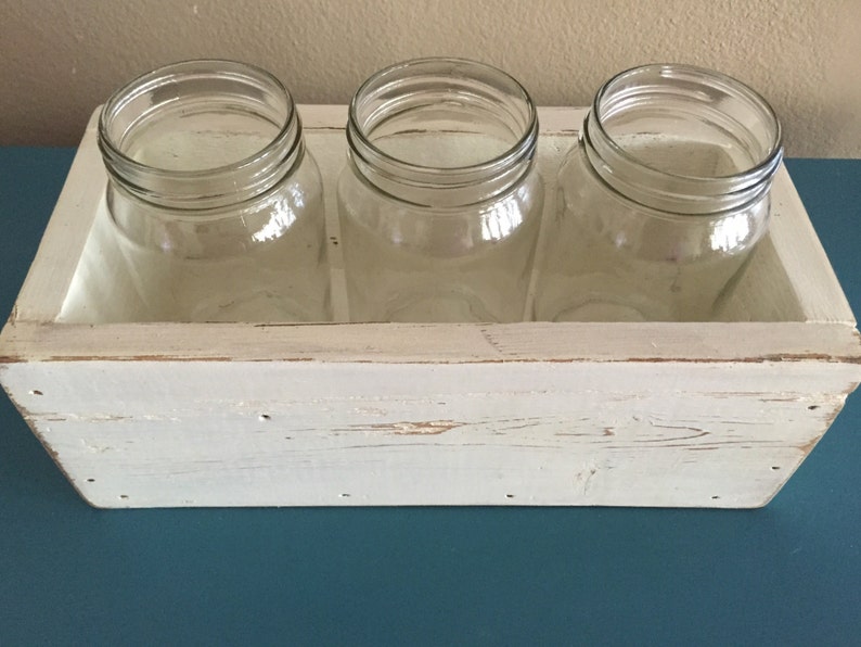 K&ouml;nnte beinhalten: Wei&szlig;e Holzkiste mit drei durchsichtigen Glasbeh&auml;ltern. Die Kiste hat eine wei&szlig;e, abgenutzte Lackierung und ist perfekt zum Pr&auml;sentieren von Blumen oder anderen Dekorationsartikeln.